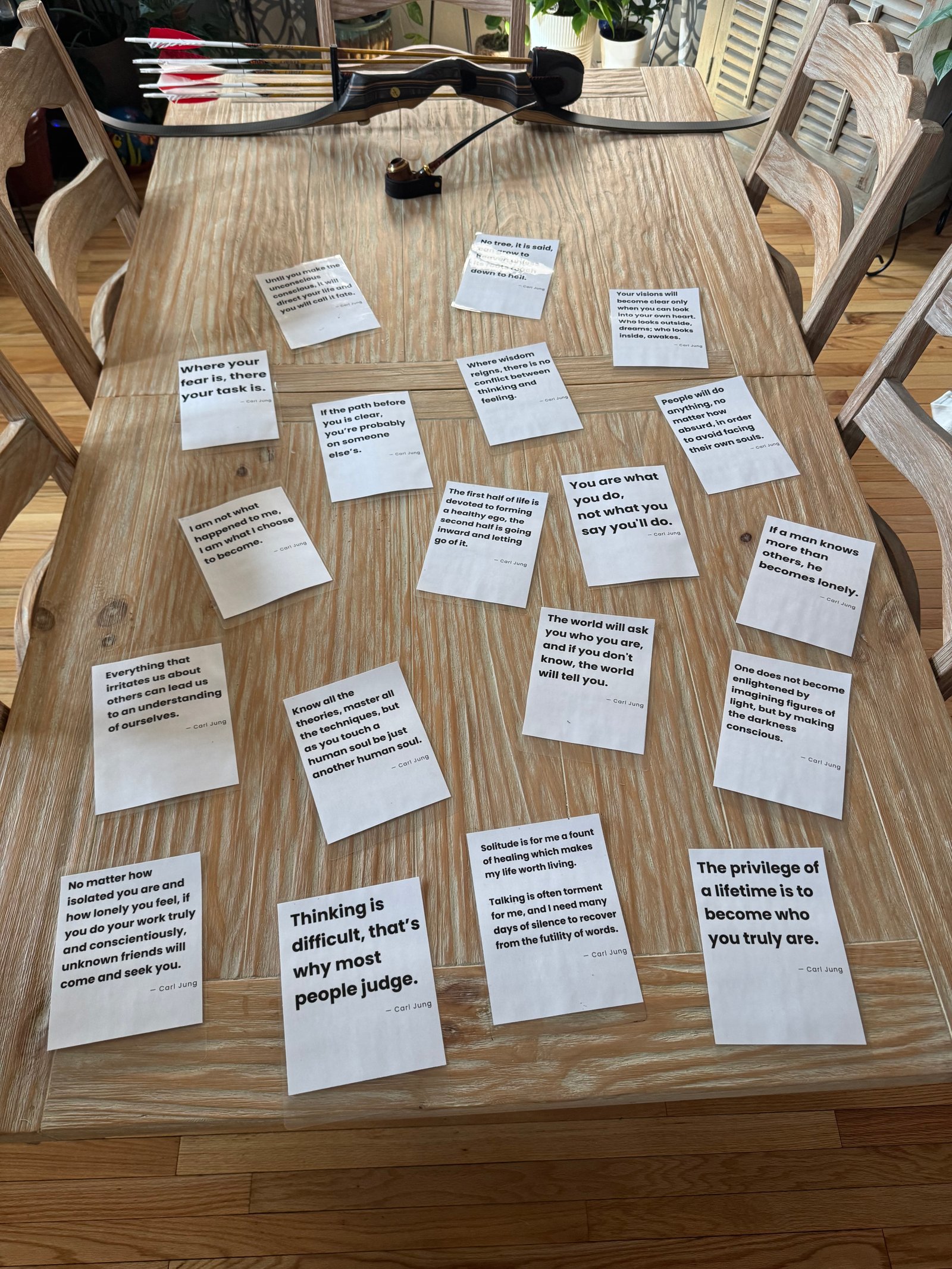 Carl Jung quote cards laid out on a wooden table, beside a recurve bow