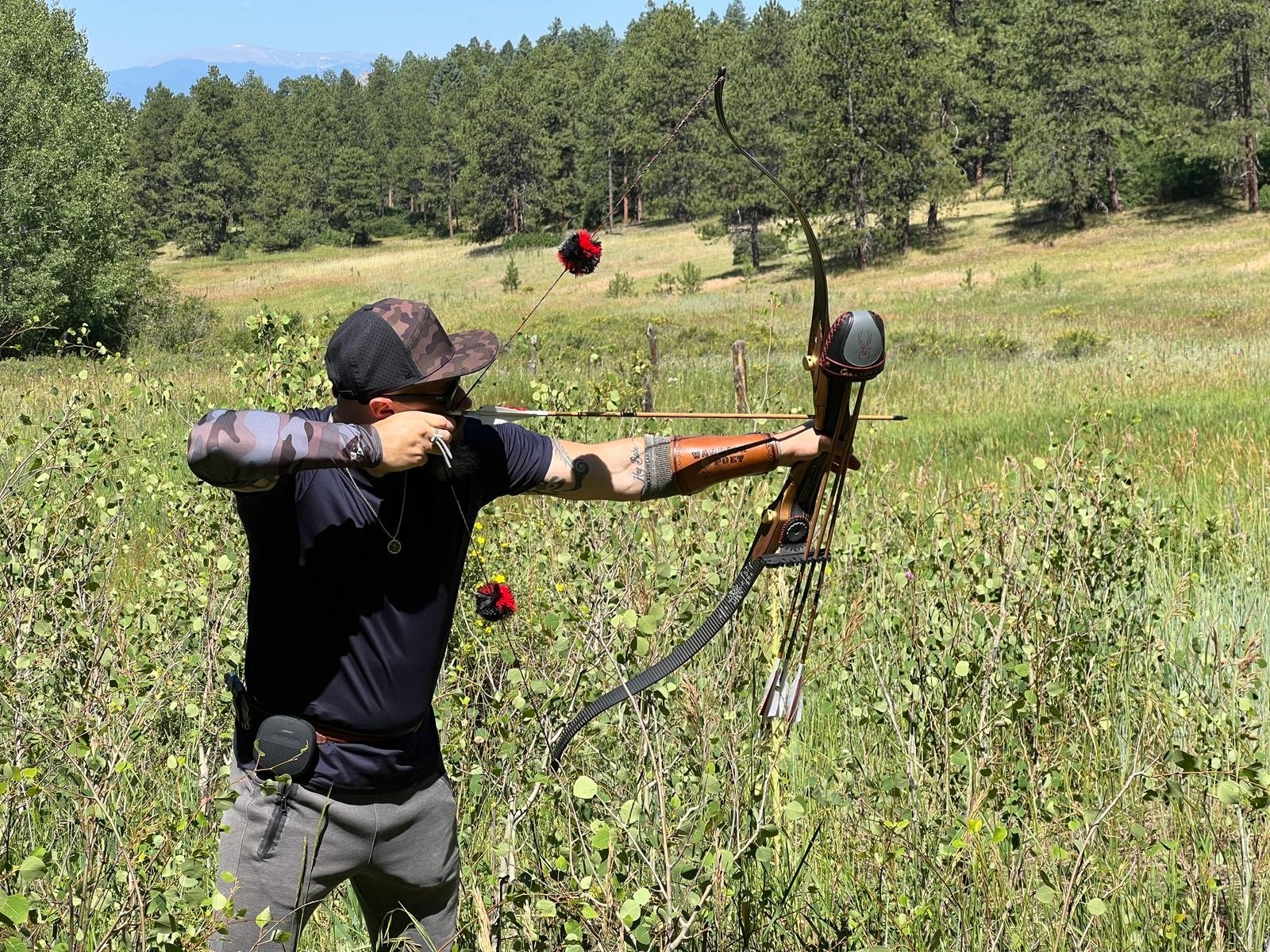 An archer at full draw in a mountain meadow